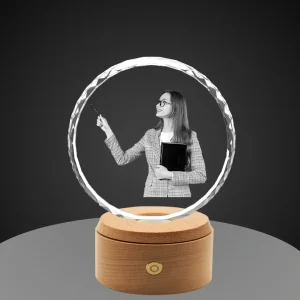 A 3D photo of a female teacher is engraved inside a round, diamond-cut crystal, a perfect appreciation gift. The crystal sits on an illuminated wooden base against a minimalist grey background.