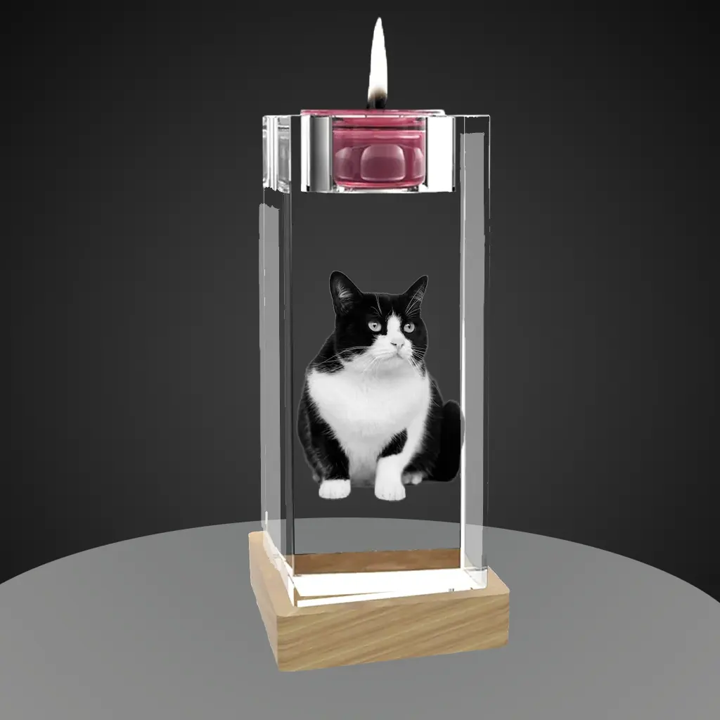 A candlestick-shaped crystal holding a lit pink tealight candle in its top holder. Inside the crystal is a 3D laser-engraved image of a black and white tuxedo cat. The crystal candlestick sits on a light-colored wooden LED base against a dark gray background.