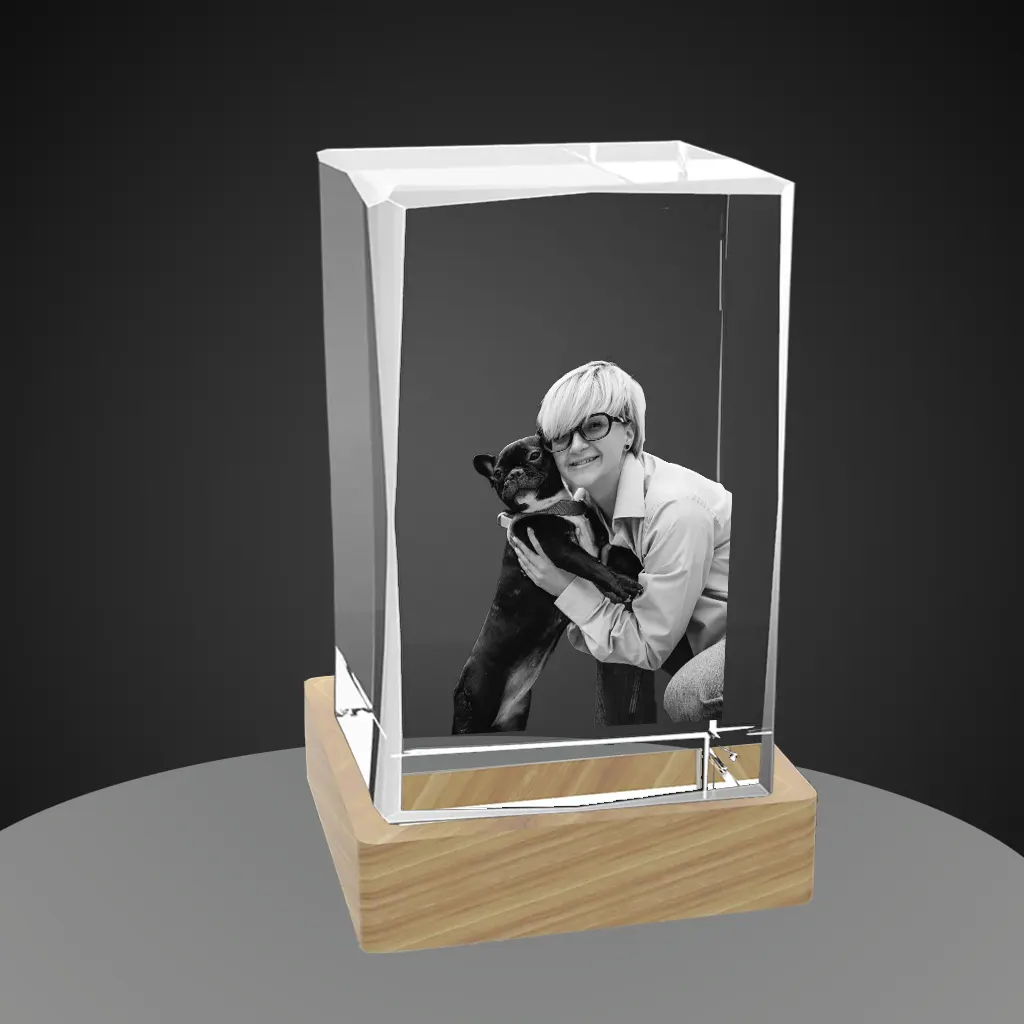 A beveled rectangular crystal with a 3D laser-engraved photo of a blonde woman with glasses and her dark pet dog, placed on a light-colored wooden LED base against a dark gray background.