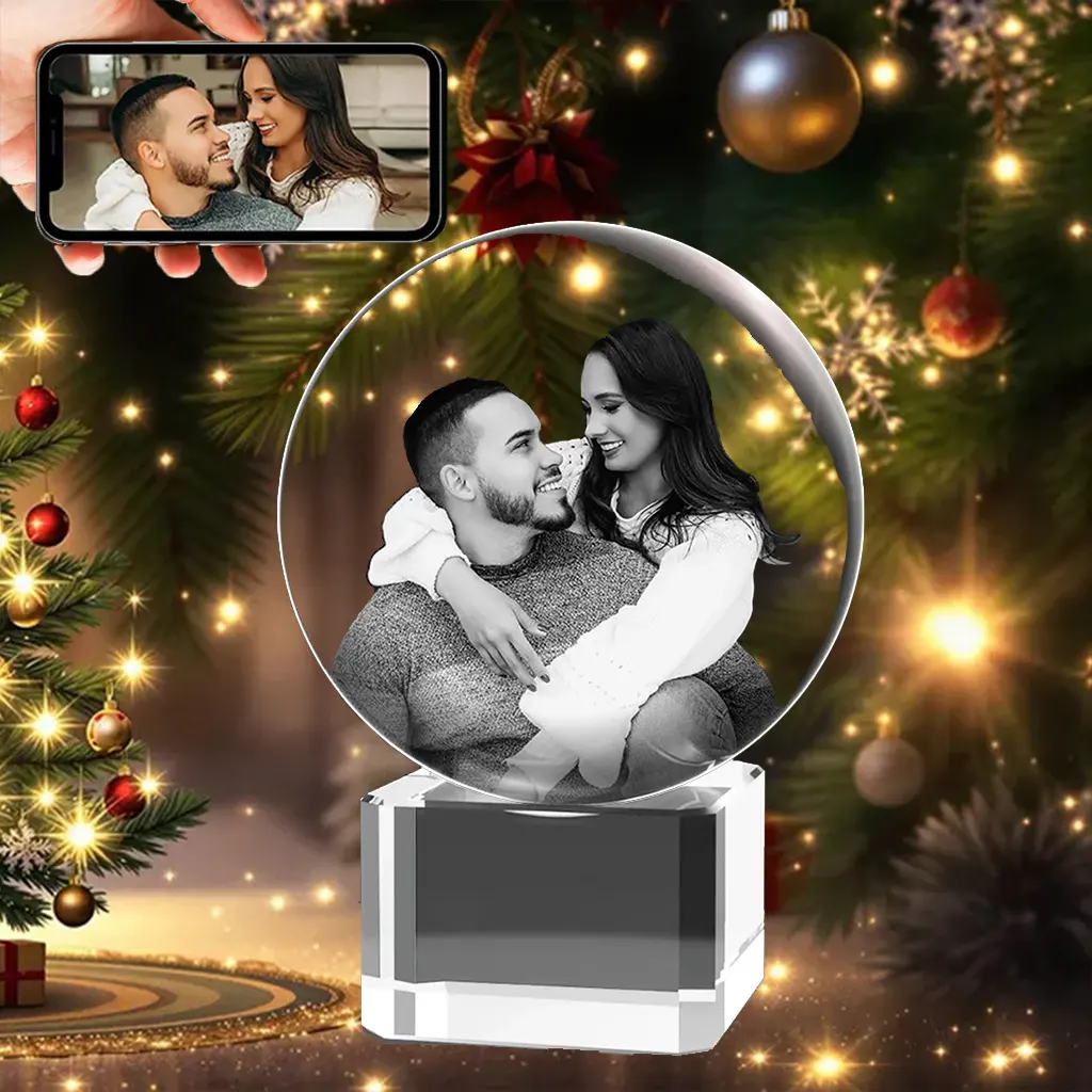 A 3D photo crystal ball engraved with a portrait of a loving couple, resting on a solid, engravable crystal base, presented as a magical Christmas gift in front of a festive tree.