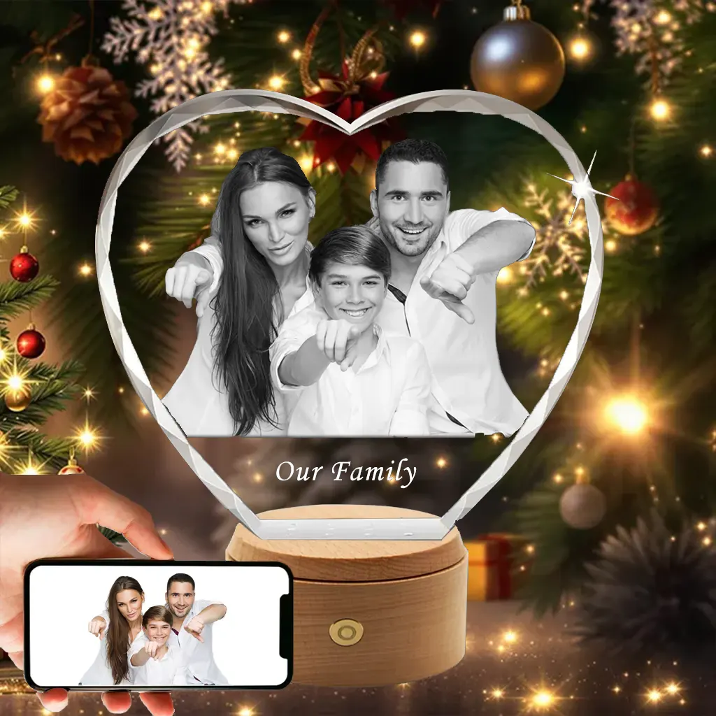 A diamond-cut heart-shaped 3D crystal, engraved with a fun photo of a family of three and the text "Our Family," presented as a joyful Christmas gift in front of a festive tree.