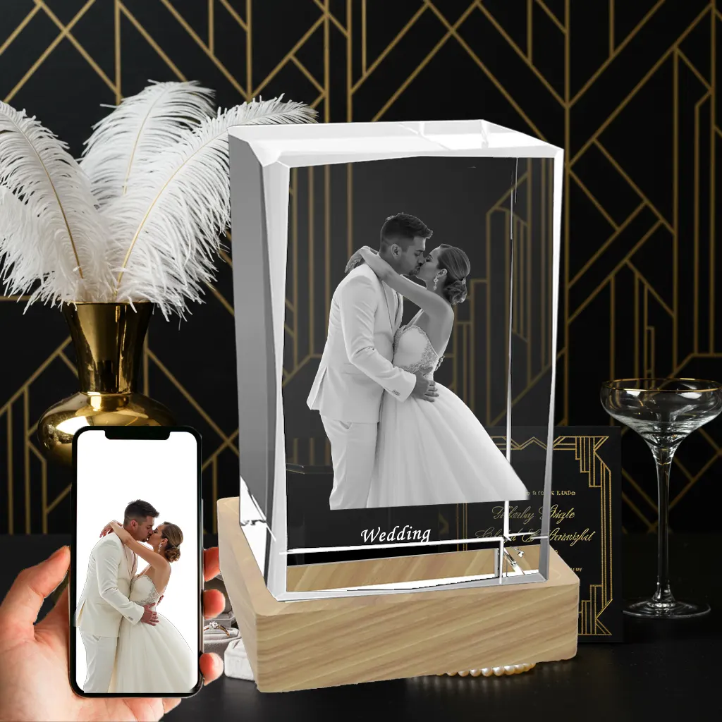 A 3D photo of a newlywed couple kissing is laser-engraved in a rectangular crystal block with the word "Wedding" below it. The crystal sits on a wooden LED base, next to a phone showing the original color photo, against a black and gold art deco background.