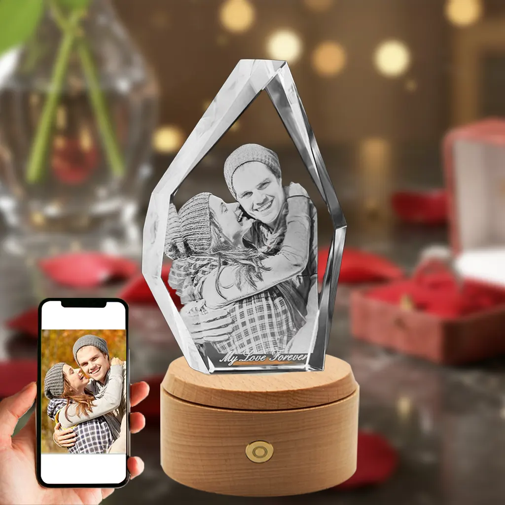 An iceberg-shaped 3D crystal engraved with a sweet photo of a hugging couple and the text "My Love Forever." The crystal is set on a rotating, illuminated wooden LED base against a romantic red rose background, with a phone in the bottom-left showing the original color photo.