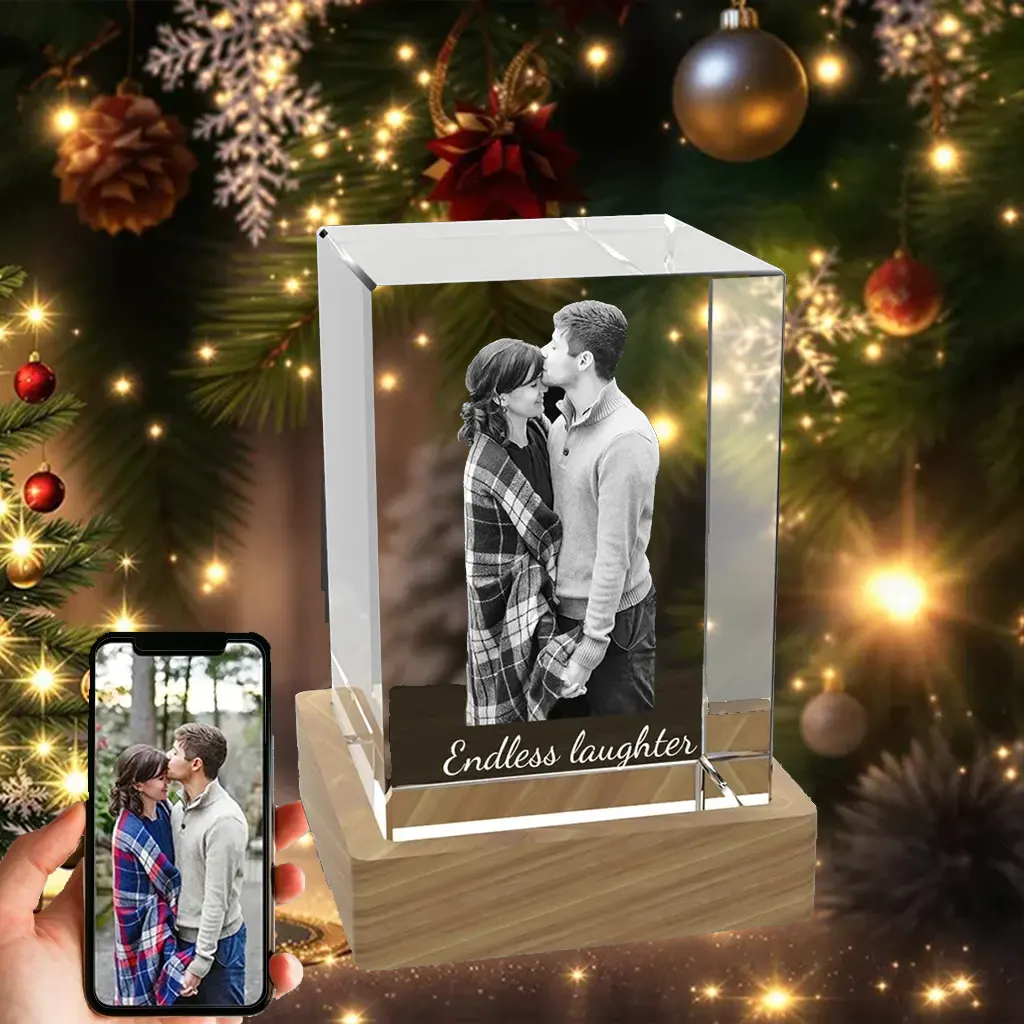 A vertical rectangular 3D crystal engraved with a tender couple's portrait and "Endless laughter," displayed as a romantic Christmas gift in front of a festive tree.