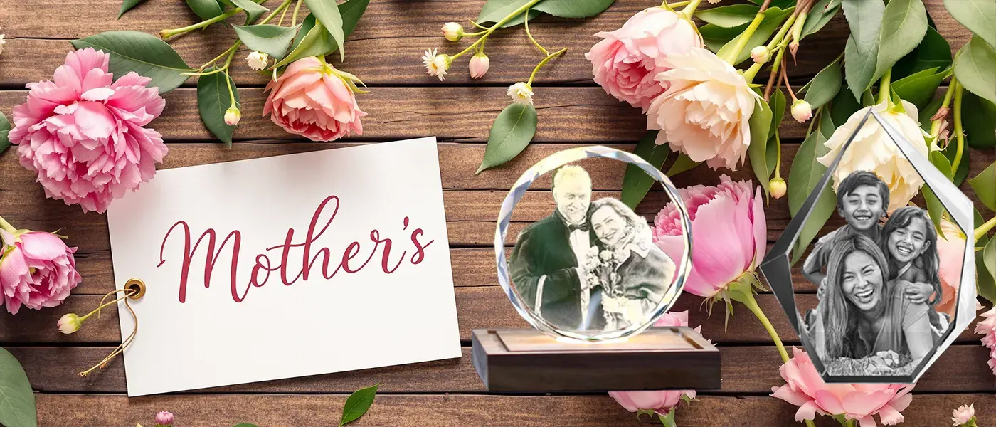 A beautiful Mother's Day flat lay with a 'Mother's' Day card, pink flowers, and two personalized 3D photo crystal gifts displaying cherished family photos on a rustic wood background.