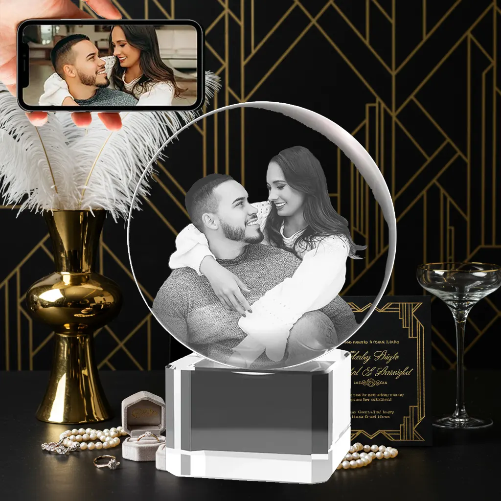A 3D photo of a smiling couple embracing is engraved inside a crystal sphere, which sits on a clear crystal base. In the upper left, a hand holds a phone showing the original color photo, all set against an elegant wedding-themed background.