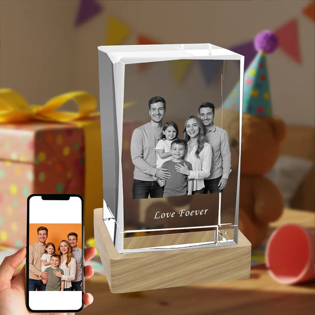 A rectangular 3D photo crystal gift on a wooden LED base, featuring a laser-etched family portrait inside. The crystal is engraved with "Love Foever." A hand holds a smartphone displaying the original color photo, set against a festive birthday party background.