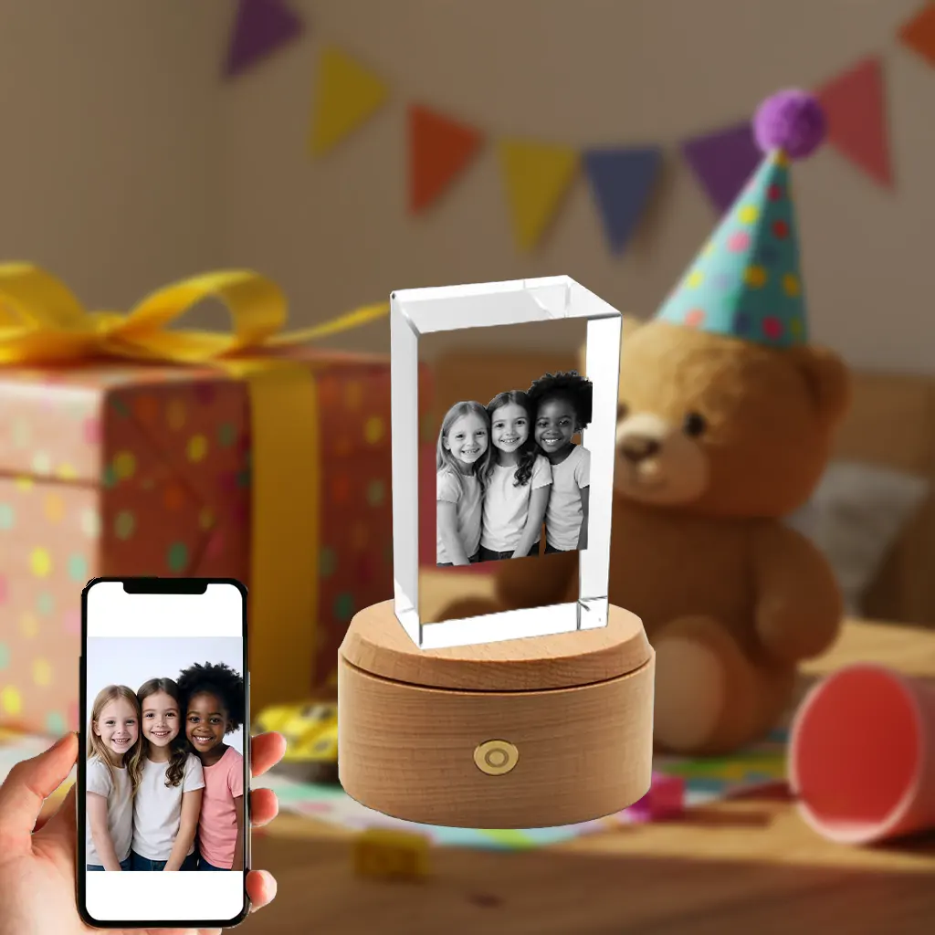 A personalized rectangular 3D photo crystal gift for children, showing an engraved picture of three young friends. The crystal is set on a rotating wooden base with LED lights. In the foreground, a smartphone displays the original color photo against a festive birthday party background.