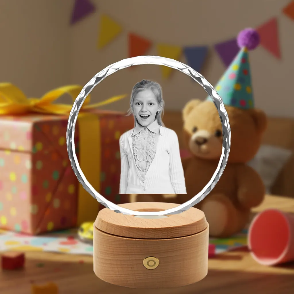 A personalized sunflower-shaped 3D photo crystal with a diamond-cut edge, showcasing a laser-etched photo of a smiling young girl. It rests on a wooden base with an LED light, set against a colorful birthday party background with a gift and a teddy bear.