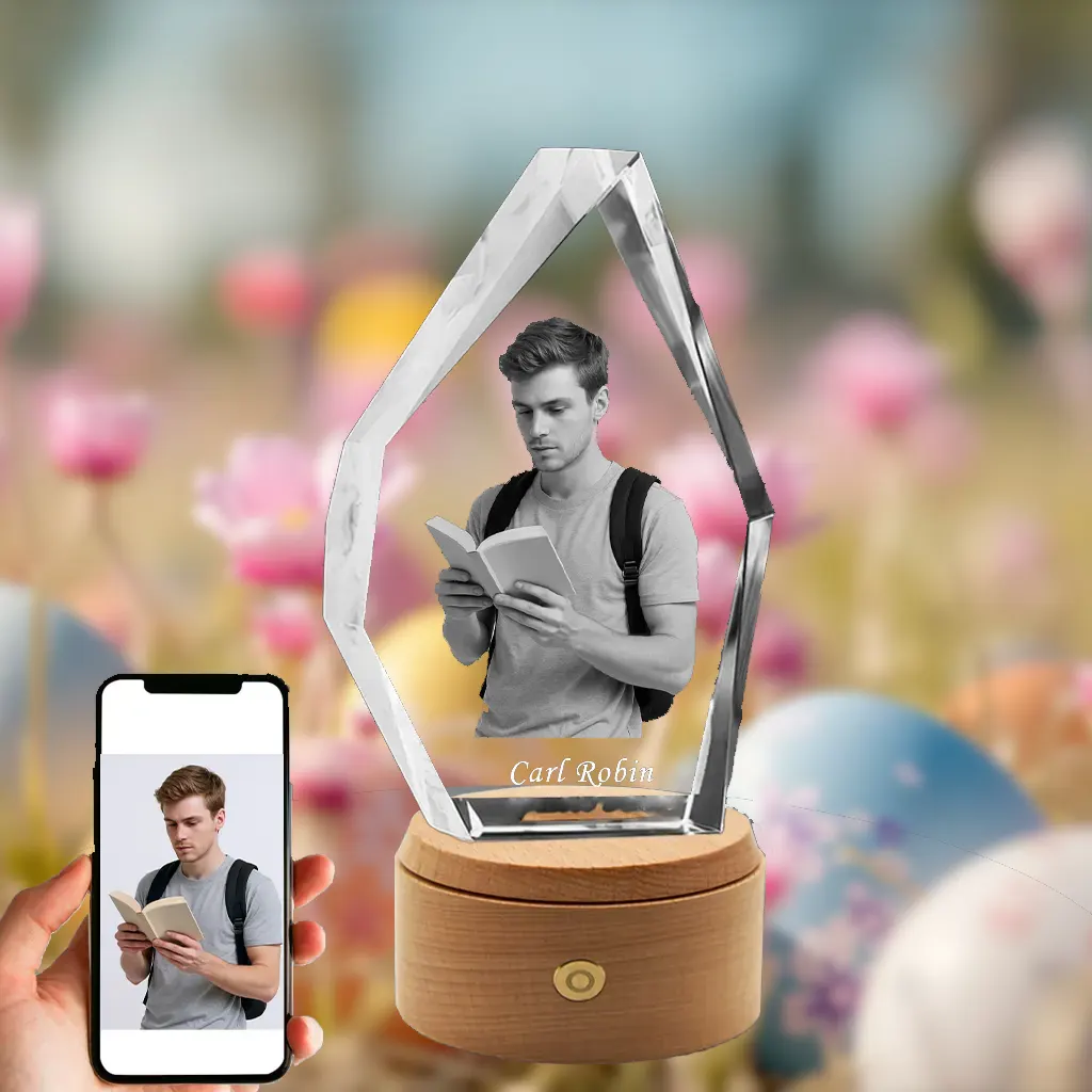 A 3D photo of a young man reading a book is engraved in a faceted, iceberg-shaped crystal with the name 'Carl Robin'. It sits on a wooden rotating LED base against a festive Easter background of flowers and eggs, with a phone showing the original photo.