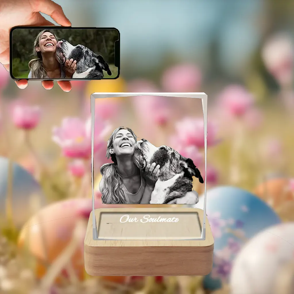 A 3D photo of a woman laughing while her dog licks her face is engraved in a rectangular crystal with 'Our Soulmate' text. It's on a wooden LED base, set against a festive Easter background of flowers and eggs, with a phone showing the original photo.