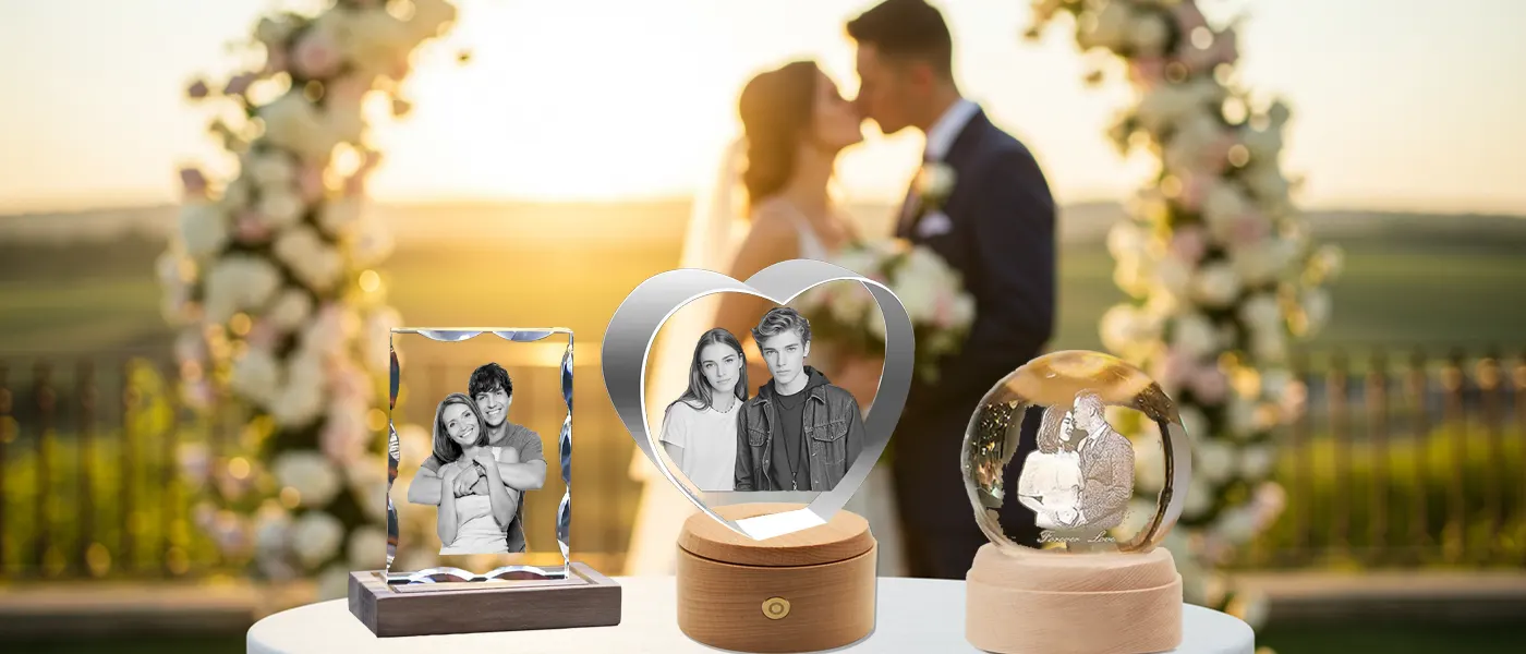 A collection of personalized 3D photo crystal gifts, including a heart and a sphere, set against a romantic sunset wedding scene with a bride and groom kissing under a floral arch.