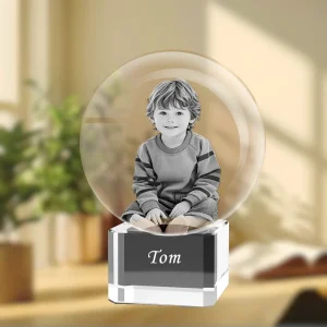 A YiYues personalized 3D crystal ball featuring a custom 3D photo of a young boy, resting on a square crystal base engraved with the name 'Tom'.