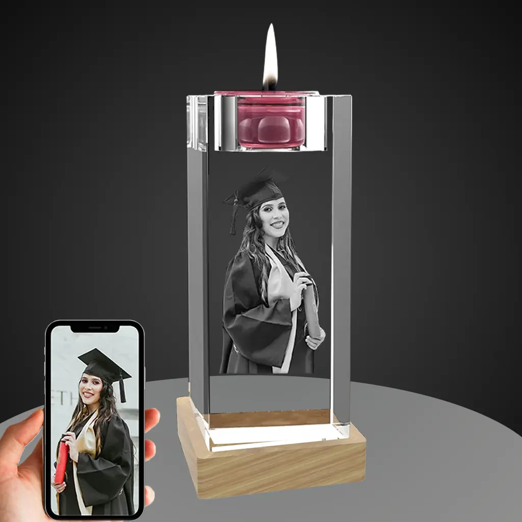 A personalized YiYues 3D crystal candle holder with a lit candle, featuring a custom photo of a female graduate. The lighted wooden base provides illumination, and a smartphone shows the original color source photo.