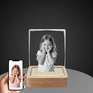 A YiYues personalized 3D deckle-edge crystal block featuring a custom photo of a smiling young girl, with 'My Love' engraved on the lighted wooden base, shown next to a smartphone displaying the original color photo.