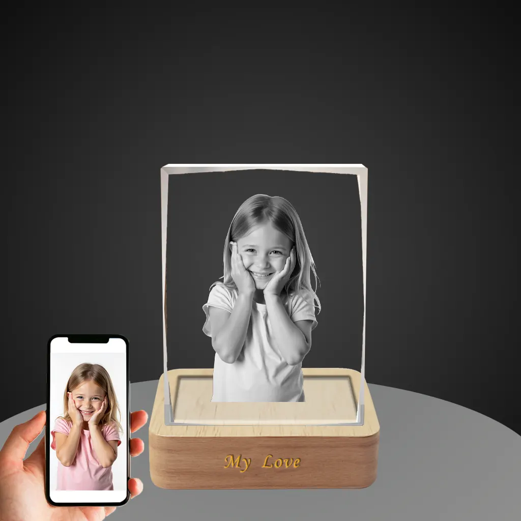 A YiYues personalized 3D deckle-edge crystal block featuring a custom photo of a smiling young girl, with 'My Love' engraved on the lighted wooden base, shown next to a smartphone displaying the original color photo.
