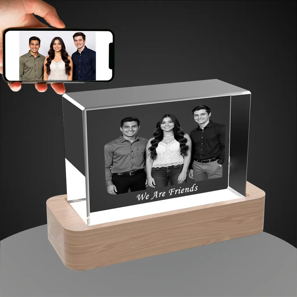 A YiYues personalized horizontal 3D crystal block featuring a custom photo of three friends, inscribed with 'We Are Friends', on a lighted wooden base. A smartphone shows the original color source photo.